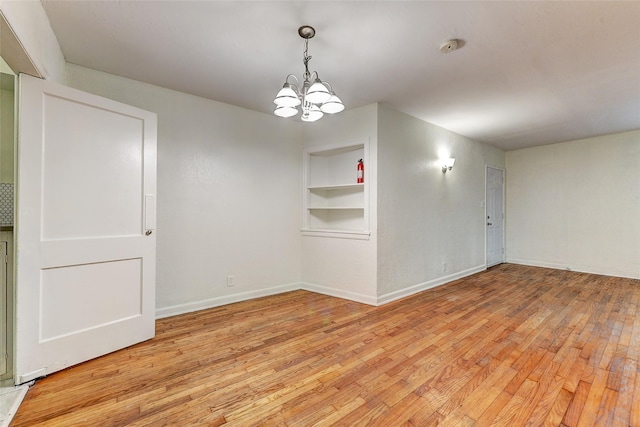 unfurnished room featuring built in features, light hardwood / wood-style floors, and an inviting chandelier