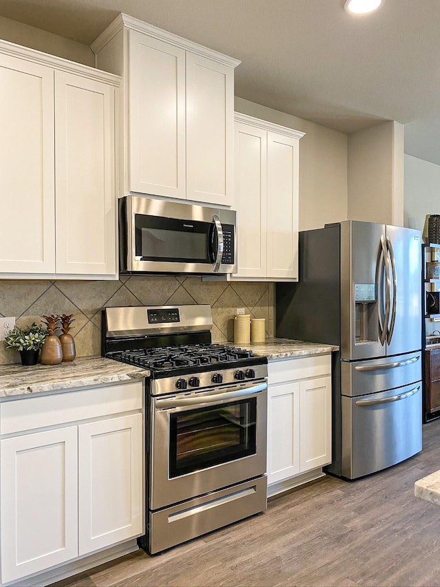 kitchen with white cabinets, appliances with stainless steel finishes, light hardwood / wood-style flooring, and light stone countertops