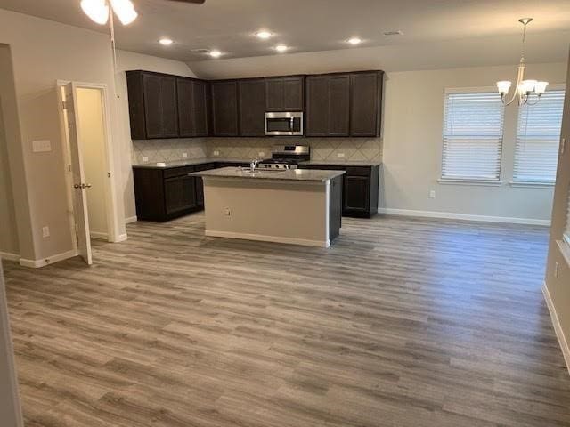 kitchen featuring appliances with stainless steel finishes, dark brown cabinetry, wood-type flooring, decorative light fixtures, and a center island with sink