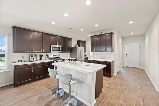 kitchen featuring dark brown cabinetry, stainless steel appliances, light hardwood / wood-style floors, a kitchen bar, and a center island with sink