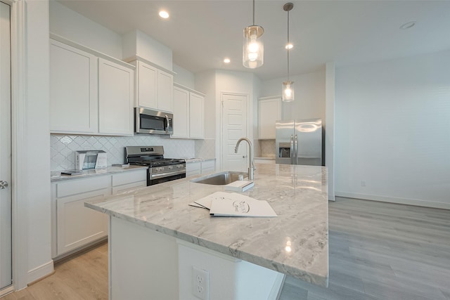 kitchen with white cabinetry, sink, stainless steel appliances, decorative light fixtures, and a center island with sink