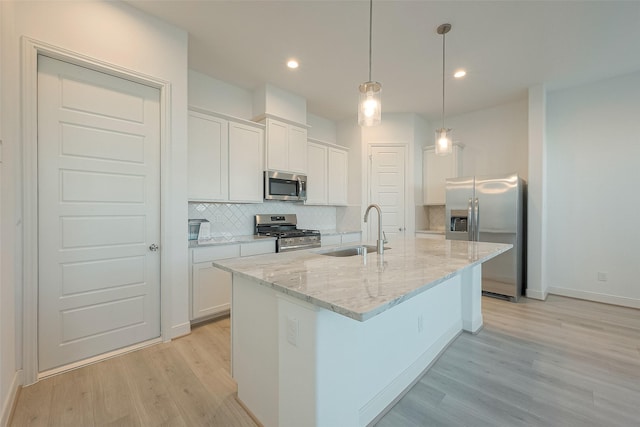 kitchen featuring stainless steel appliances, sink, decorative light fixtures, white cabinetry, and an island with sink