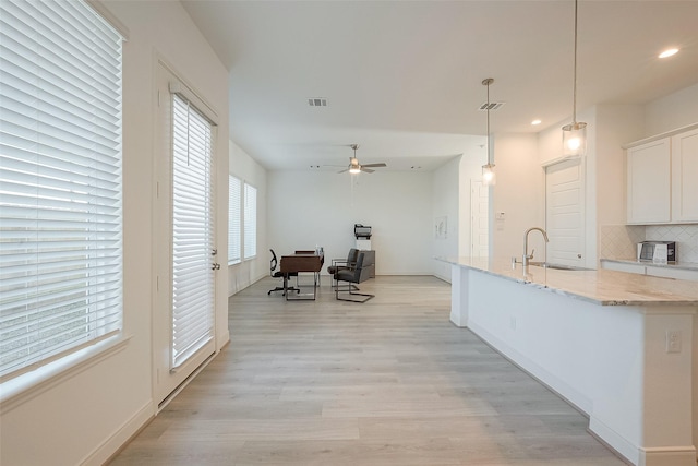 kitchen with hanging light fixtures, ceiling fan, decorative backsplash, light stone counters, and white cabinetry