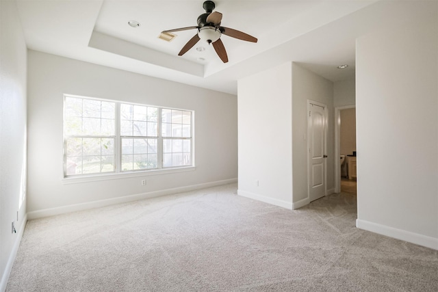 unfurnished room with ceiling fan, a raised ceiling, and light carpet