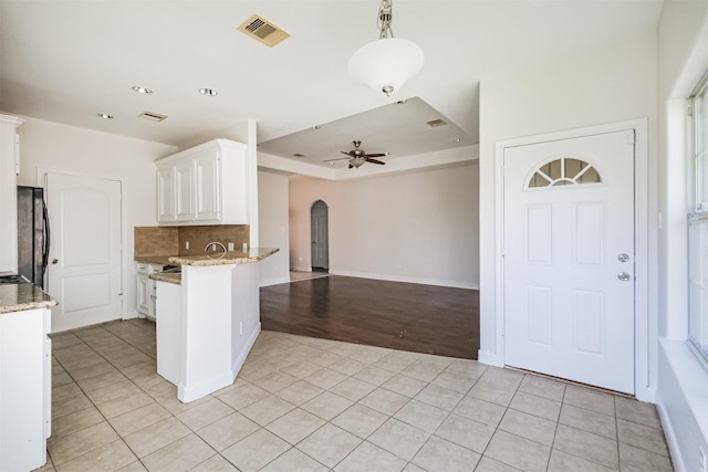 kitchen with black refrigerator, ceiling fan, light tile patterned floors, a tray ceiling, and white cabinetry