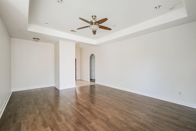 empty room with ceiling fan, dark hardwood / wood-style floors, and a tray ceiling