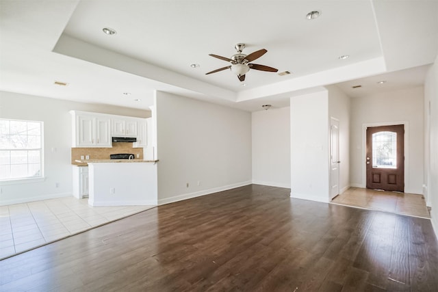 unfurnished living room featuring light hardwood / wood-style floors, a raised ceiling, and ceiling fan