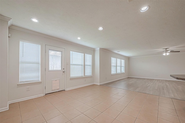 interior space featuring ceiling fan, ornamental molding, a textured ceiling, and light tile patterned floors