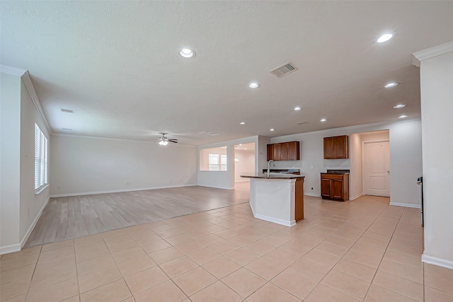 kitchen with ceiling fan, light tile patterned floors, an island with sink, and ornamental molding