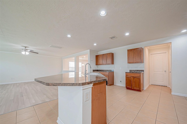 kitchen featuring a kitchen island with sink, sink, ceiling fan, ornamental molding, and light tile patterned floors