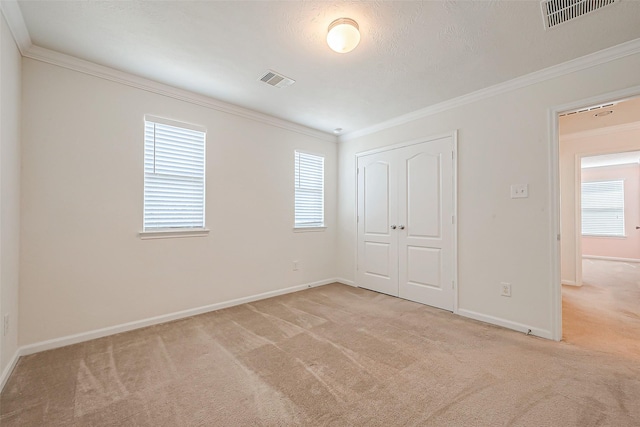 unfurnished bedroom featuring a textured ceiling, crown molding, light carpet, and a closet