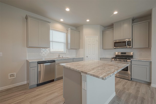 kitchen with appliances with stainless steel finishes, light hardwood / wood-style floors, a kitchen island, and gray cabinetry