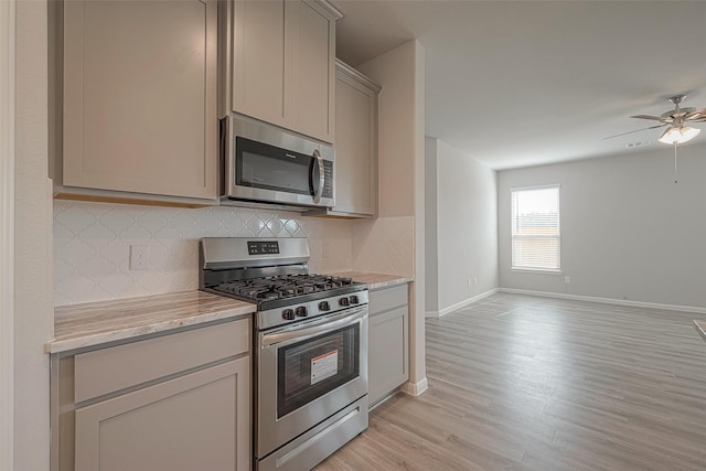 kitchen featuring gray cabinetry, light stone countertops, ceiling fan, stainless steel appliances, and light hardwood / wood-style flooring