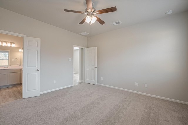 unfurnished bedroom featuring ceiling fan, ensuite bathroom, and light carpet