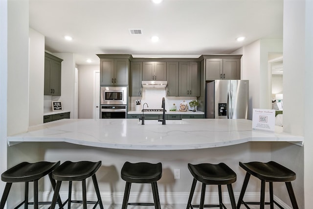 kitchen featuring kitchen peninsula, a breakfast bar, stainless steel appliances, and light stone counters