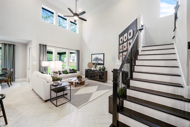 living area with baseboards, ceiling fan, stairway, and a towering ceiling