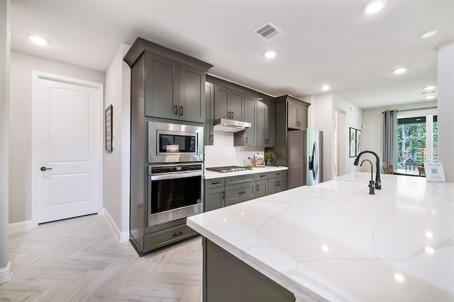 kitchen with light stone counters, recessed lighting, under cabinet range hood, stainless steel appliances, and visible vents