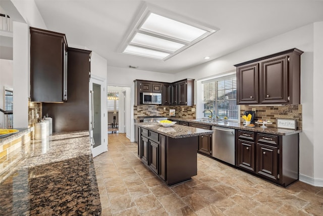 kitchen with a center island, stainless steel appliances, dark brown cabinetry, and dark stone counters