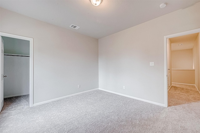 unfurnished bedroom with a walk in closet, a closet, and light carpet