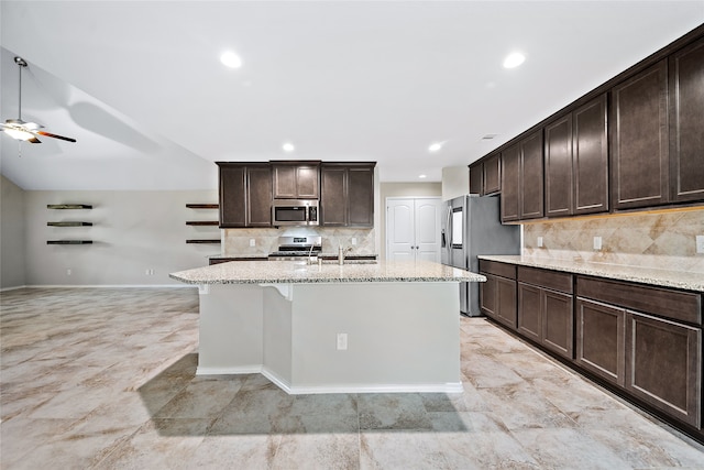 kitchen with light stone countertops, stainless steel appliances, an island with sink, dark brown cabinets, and sink