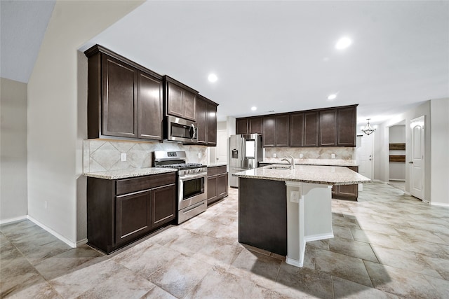 kitchen with light stone counters, stainless steel appliances, an island with sink, and sink