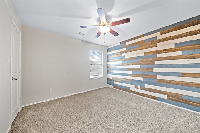 empty room featuring ceiling fan, wooden walls, and carpet floors