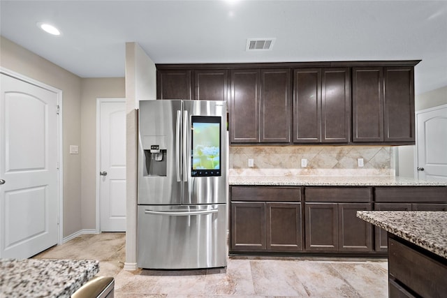 kitchen with light stone countertops, stainless steel fridge with ice dispenser, decorative backsplash, and dark brown cabinetry