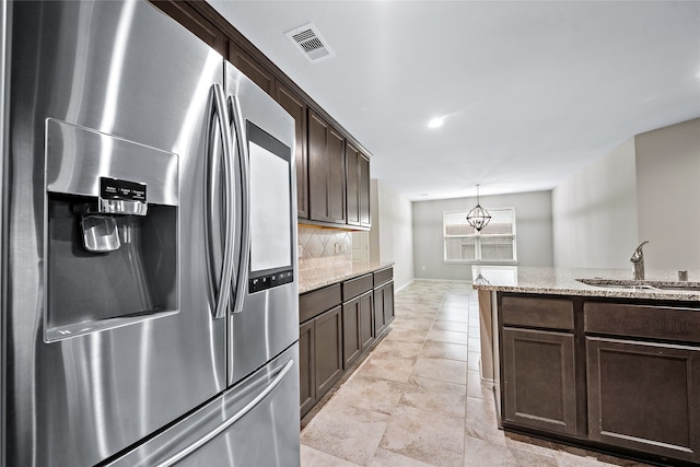 kitchen with sink, light stone counters, tasteful backsplash, dark brown cabinets, and stainless steel fridge with ice dispenser