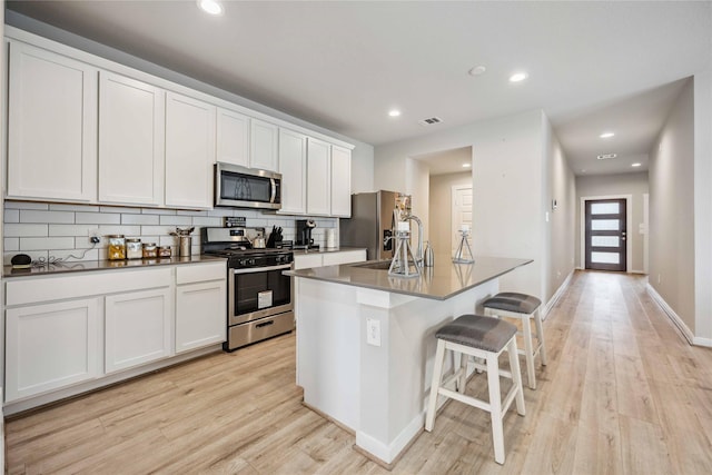 kitchen with a kitchen island with sink, white cabinets, a kitchen breakfast bar, sink, and stainless steel appliances