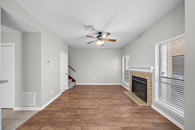 unfurnished living room featuring ceiling fan, wood-type flooring, and a brick fireplace