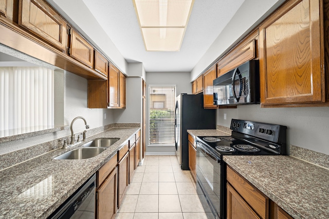 kitchen with light tile patterned floors, sink, dark stone countertops, and black appliances