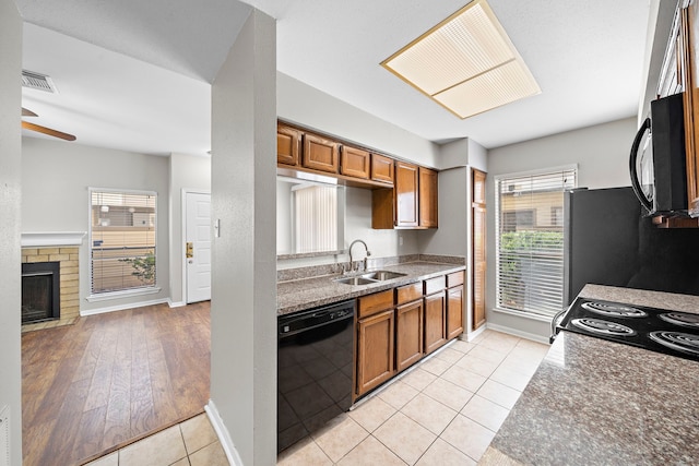 kitchen with a brick fireplace, ceiling fan, sink, black appliances, and light tile patterned floors