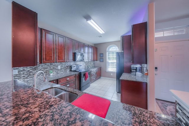 kitchen featuring sink, dark stone counters, decorative backsplash, light tile patterned flooring, and black appliances