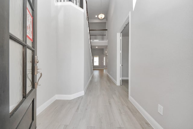 corridor with light wood-style floors, a high ceiling, and baseboards