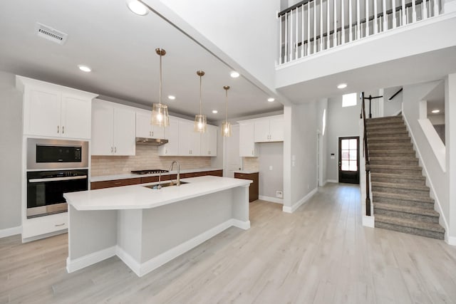 kitchen with visible vents, light wood-style flooring, a high ceiling, stainless steel appliances, and under cabinet range hood