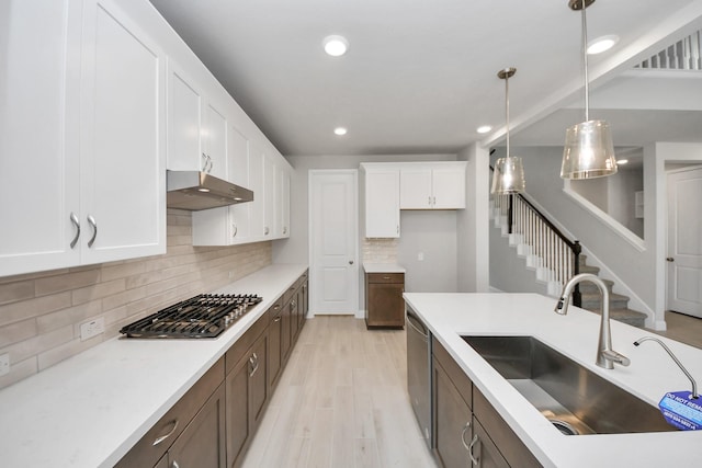 kitchen featuring under cabinet range hood, stainless steel appliances, a sink, white cabinets, and pendant lighting