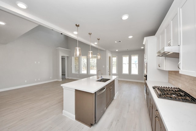 kitchen with a center island with sink, stainless steel appliances, decorative backsplash, vaulted ceiling, and under cabinet range hood