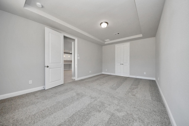 unfurnished bedroom with carpet floors, a tray ceiling, visible vents, and baseboards