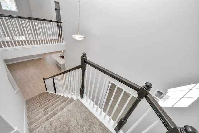 stairway with a high ceiling, wood finished floors, and visible vents