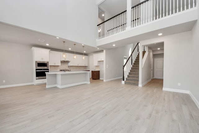 unfurnished living room featuring baseboards, recessed lighting, stairs, and light wood-style floors