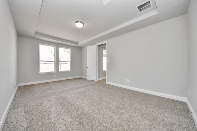 spare room featuring carpet, a raised ceiling, visible vents, and baseboards