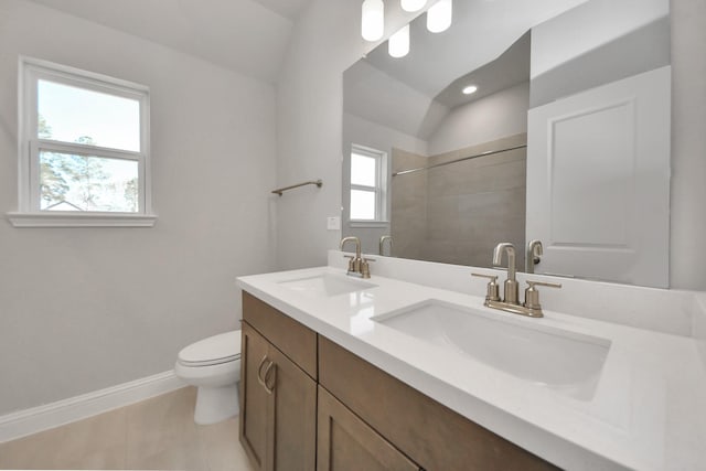 bathroom with tiled shower, a sink, toilet, and baseboards