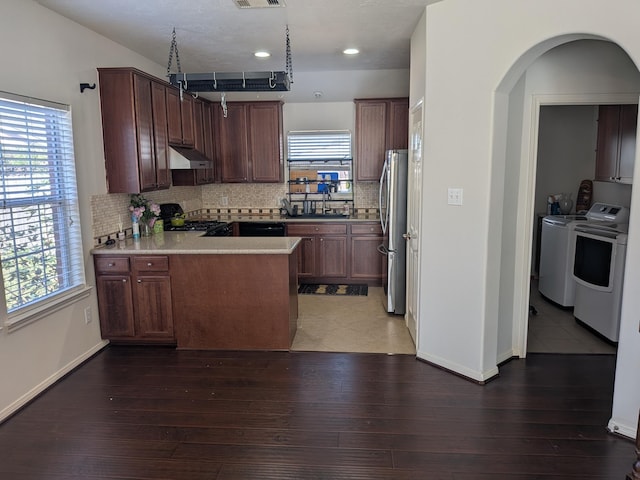 kitchen featuring independent washer and dryer, backsplash, kitchen peninsula, stainless steel fridge, and stove