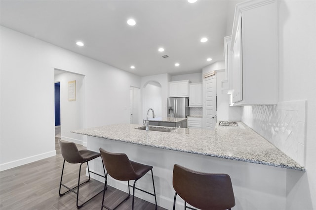 kitchen with kitchen peninsula, a breakfast bar, sink, white cabinetry, and tasteful backsplash