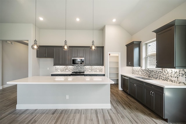 kitchen with stainless steel appliances, wood finished floors, a sink, light countertops, and a center island