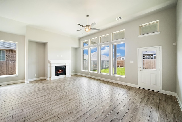 unfurnished living room featuring a warm lit fireplace, a ceiling fan, baseboards, visible vents, and light wood-style floors