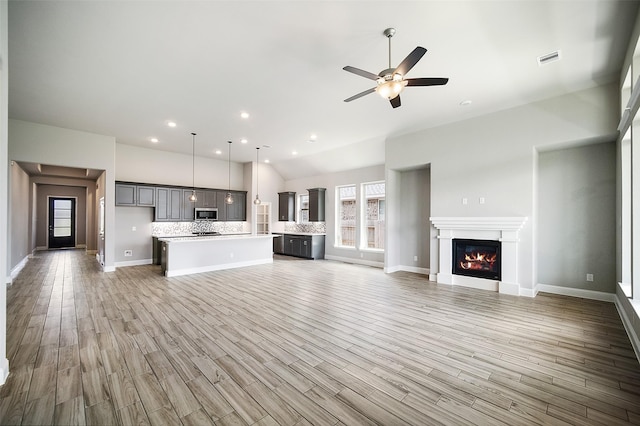 unfurnished living room featuring a ceiling fan, a glass covered fireplace, visible vents, and light wood-style floors