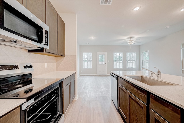 kitchen with sink, stainless steel appliances, tasteful backsplash, light stone counters, and light hardwood / wood-style floors