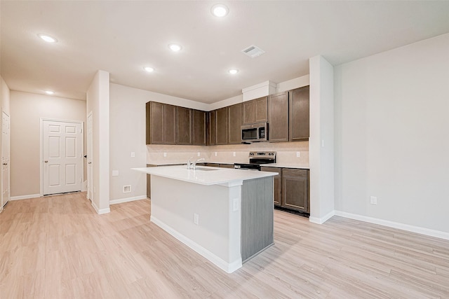 kitchen with appliances with stainless steel finishes, an island with sink, light hardwood / wood-style flooring, and backsplash