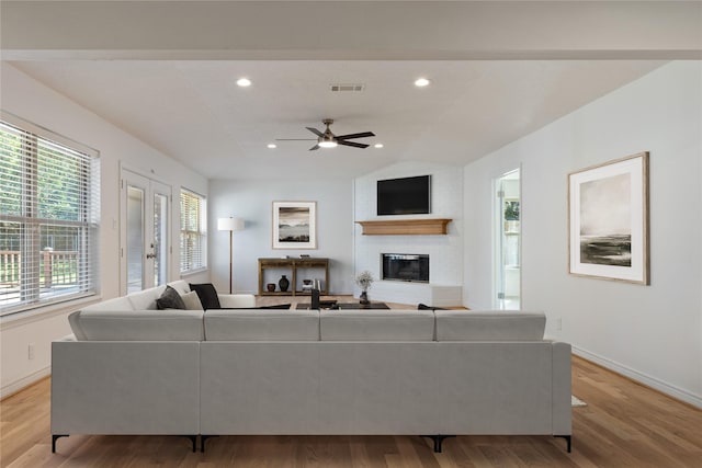 living room featuring french doors, a large fireplace, vaulted ceiling, ceiling fan, and light hardwood / wood-style flooring